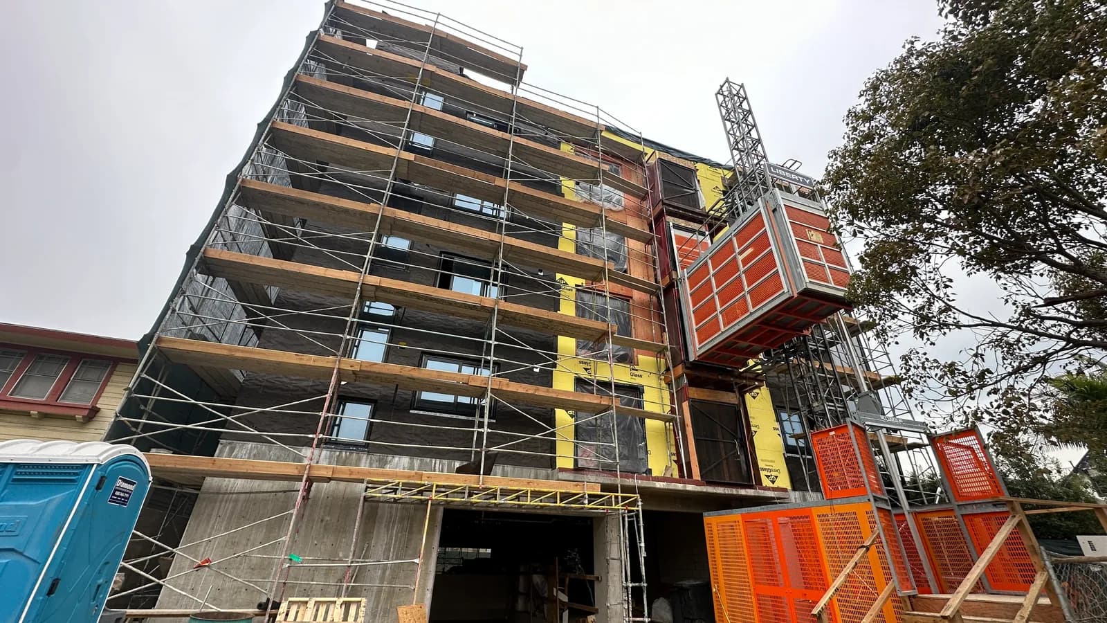 A mid-rise apartment building under construction in Los Angeles, scaffolded with a construction hoist on the elevation.