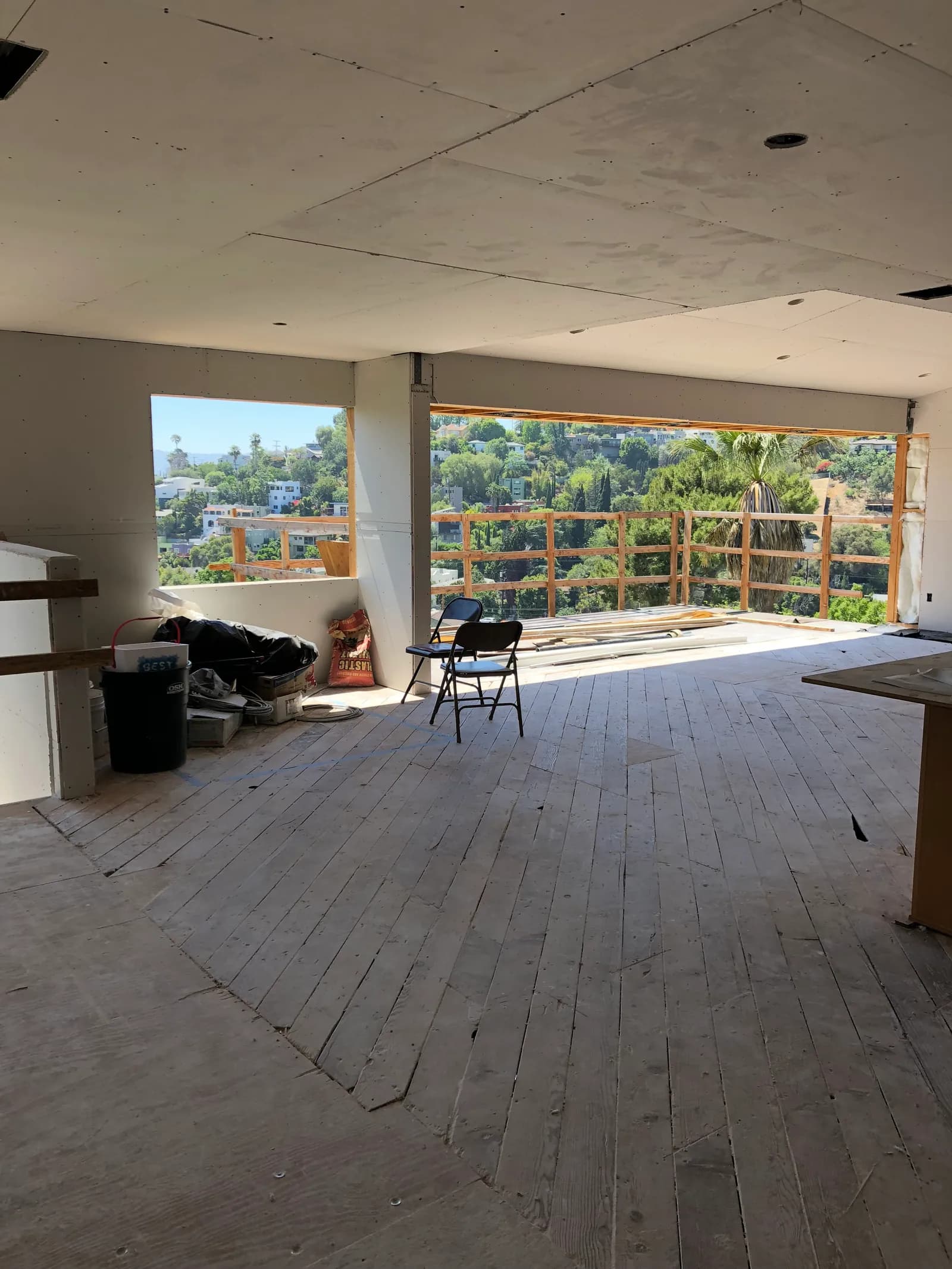 A hillside room with board hung across walls and ceiling, opening through a wide window wall onto the hills.