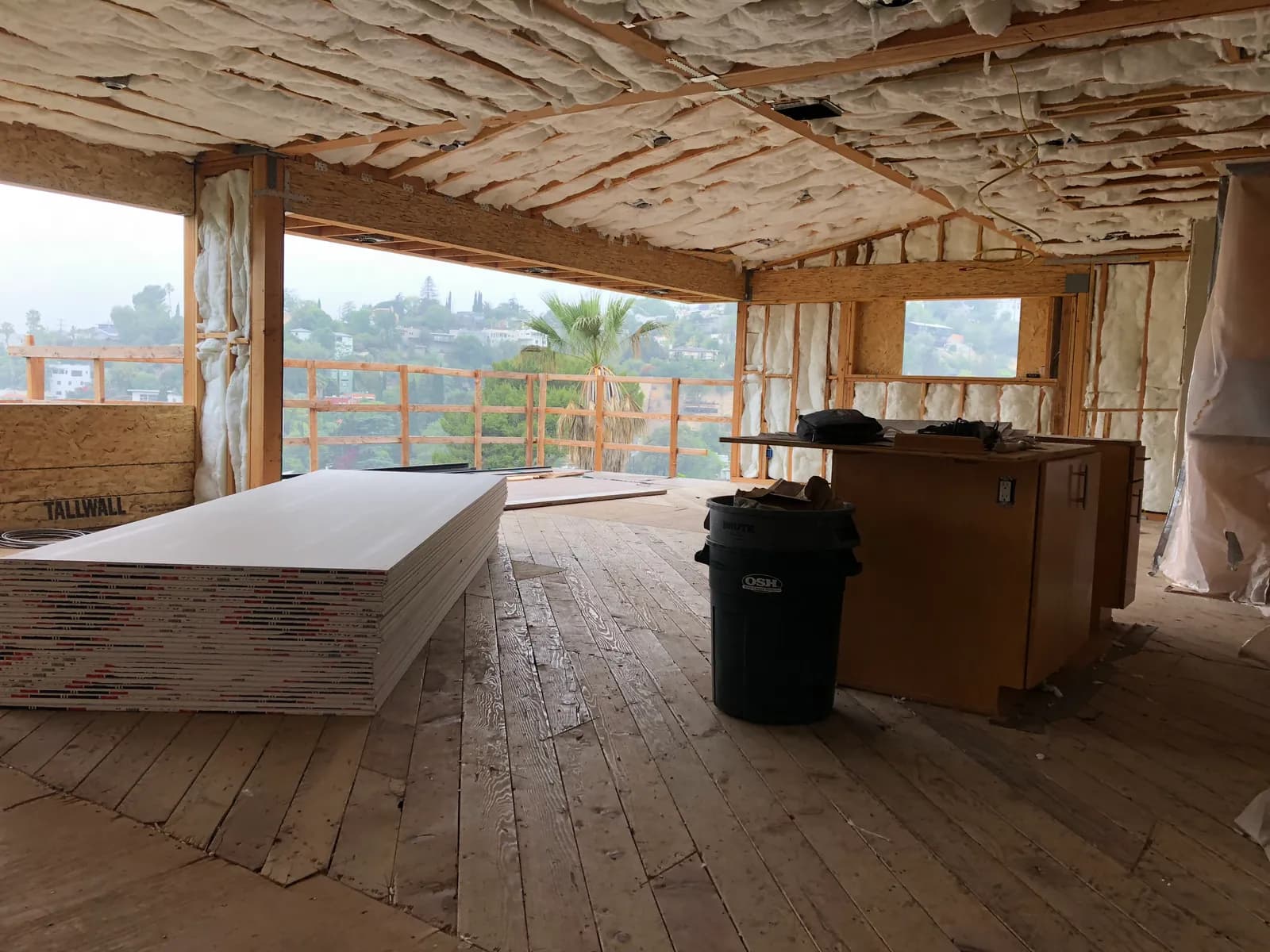 An insulated ceiling above a hillside room, board stacked on the floor.