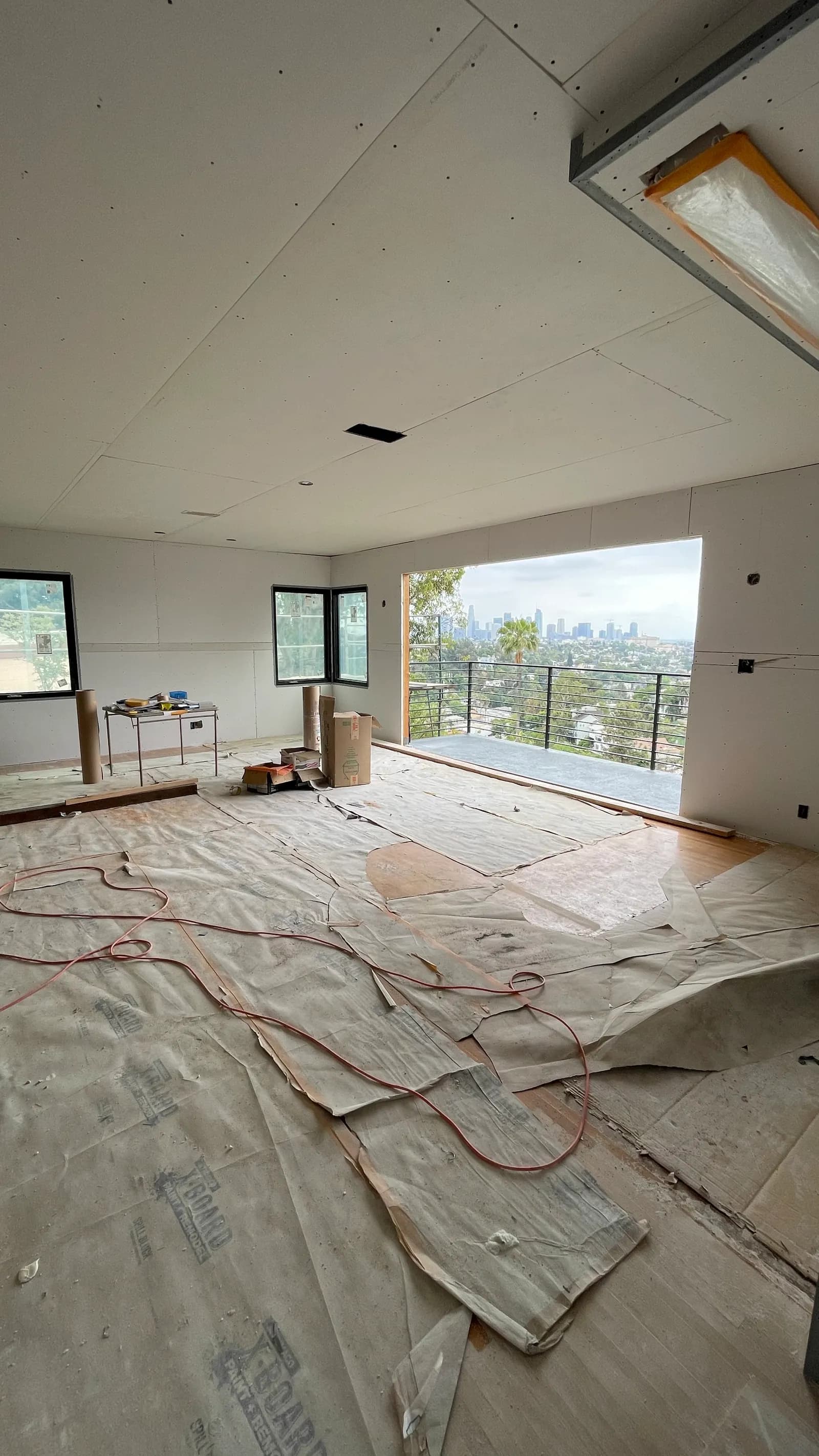 A wider view of the same hillside room with board hung across the ceiling and walls, floor papered, and tools still on site.